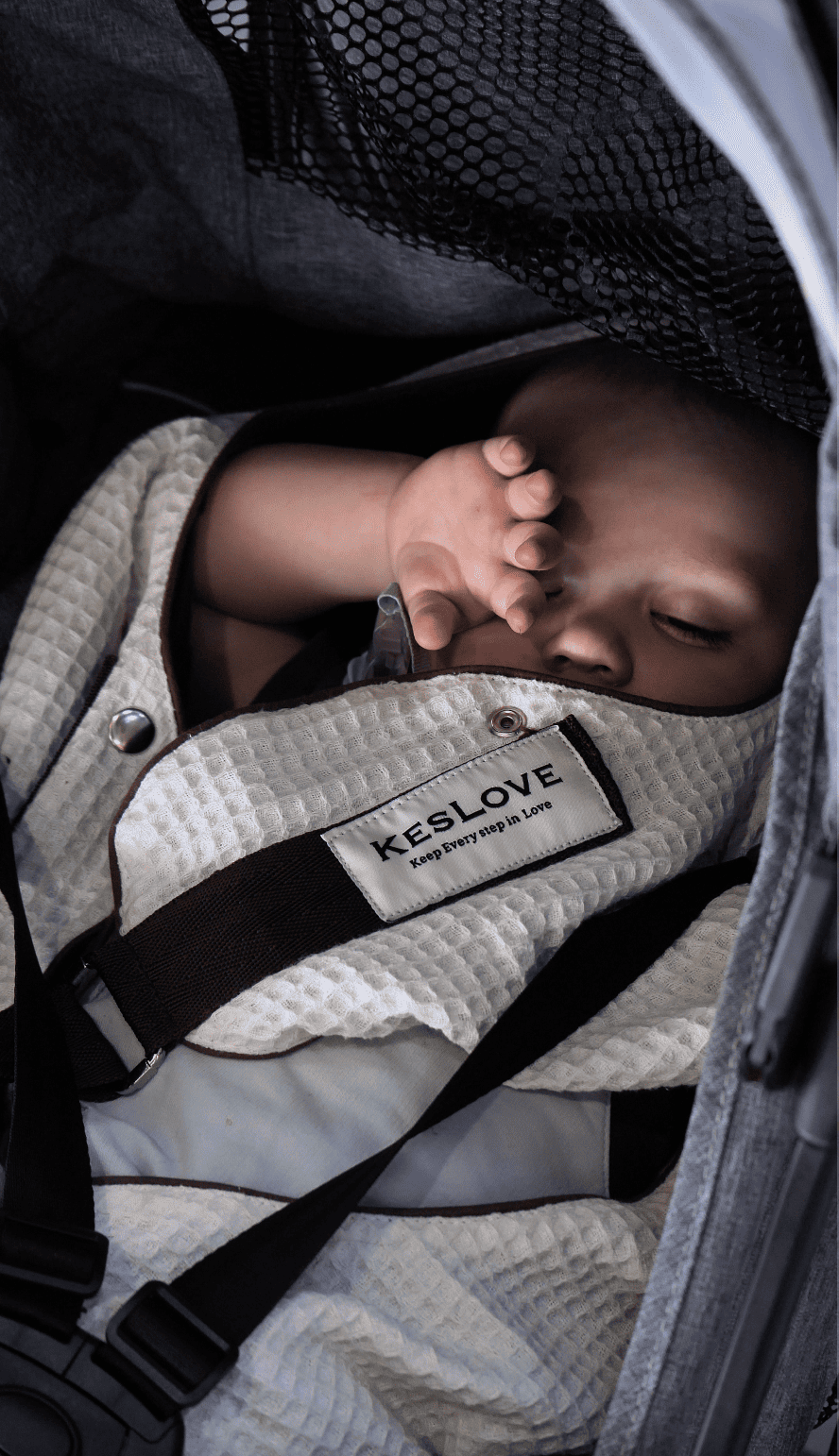 Close-up view of a napping infant comfortably secured in a KESLOVE baby carrier, showing the label.
