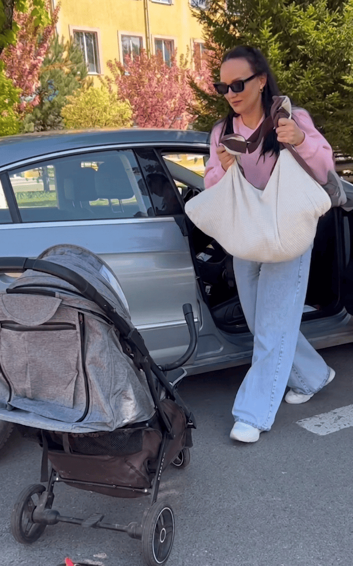 Mother comfortably using the KESLOVE carrier while handling a folded stroller by her car.
